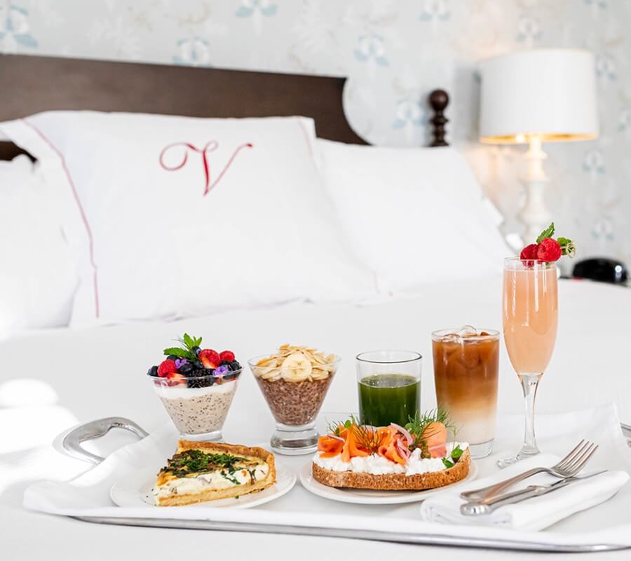 tray containing fruit cup, toast and other breakfast items sitting atop a guest room bed with white sheets